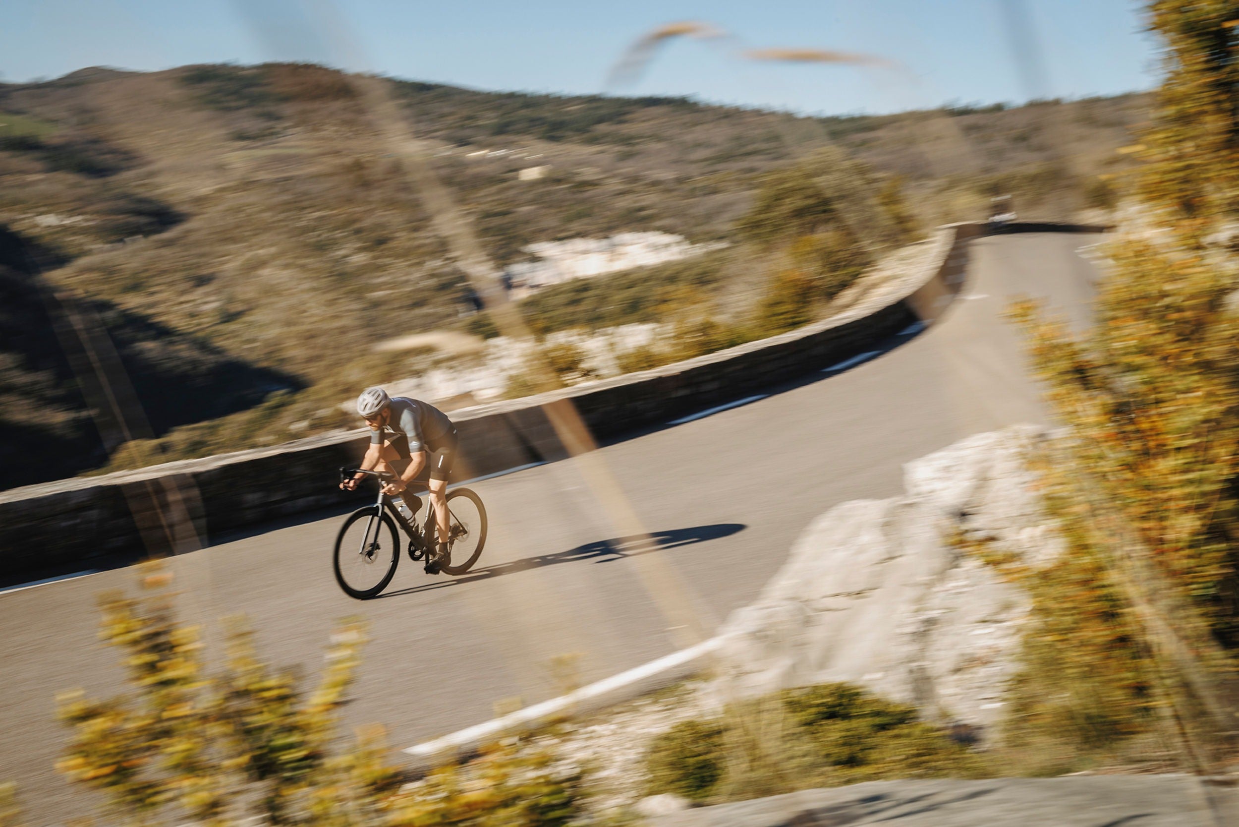 Person cycling on road bike on a winding road with scenic hills in the background