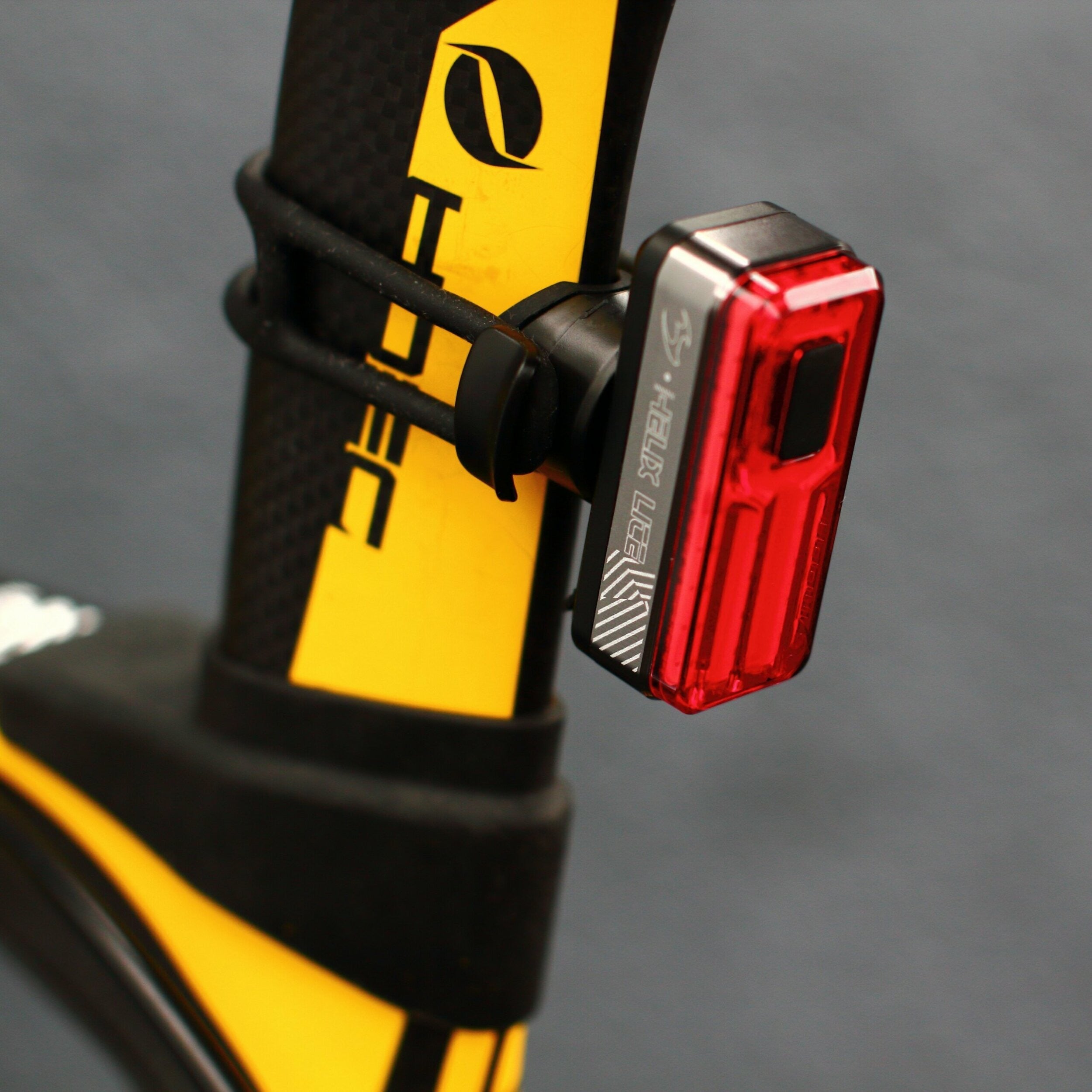 Red bicycle tail light attached to a yellow and black bike frame.