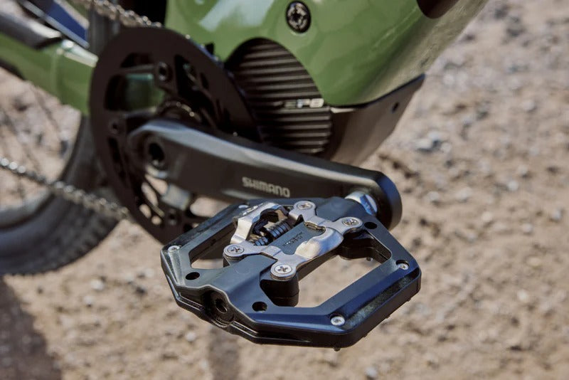 Close-up of a bicycle pedal with chain and gear system on a gravel surface