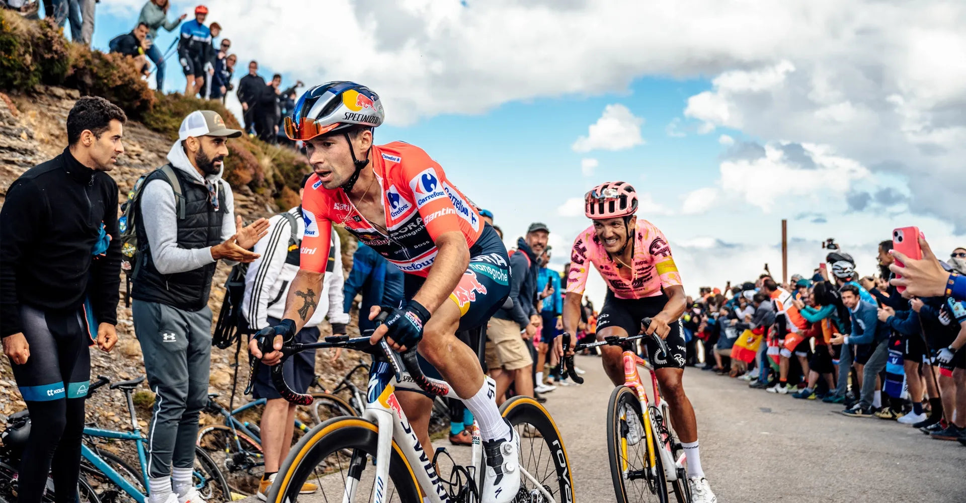 Cyclists racing on a mountain road with spectators and other cyclists in the background.