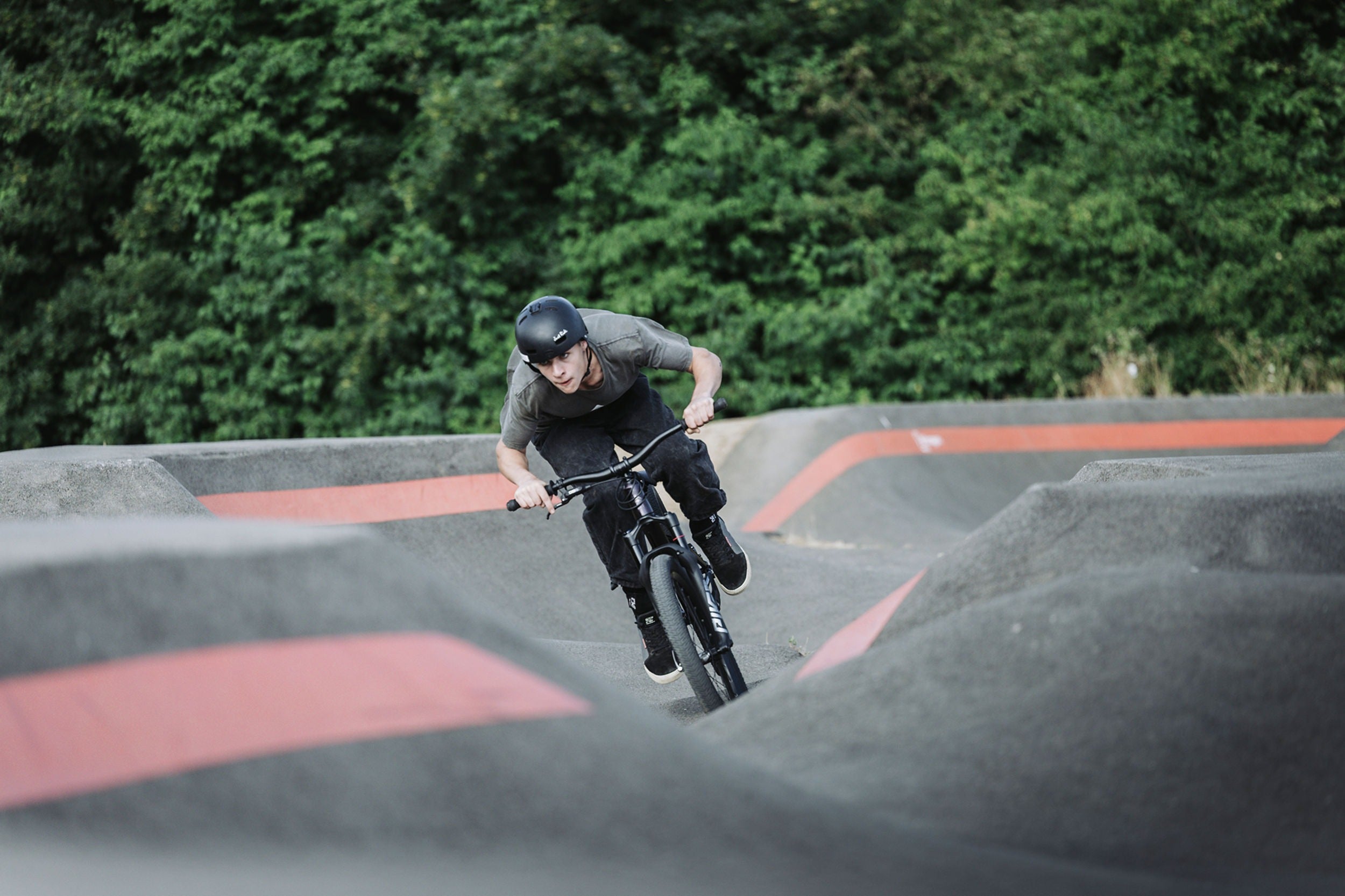 Person riding a dirt jump bike at a bmx track with trees in the background