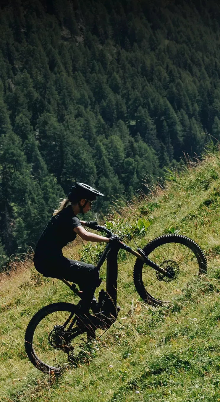 Person riding a mountain bike on a grassy hill with a forest in the background