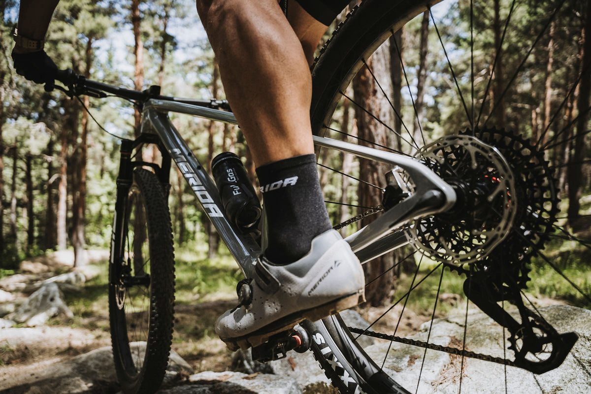Person riding a Merida mountain bike on a trail with trees in the background