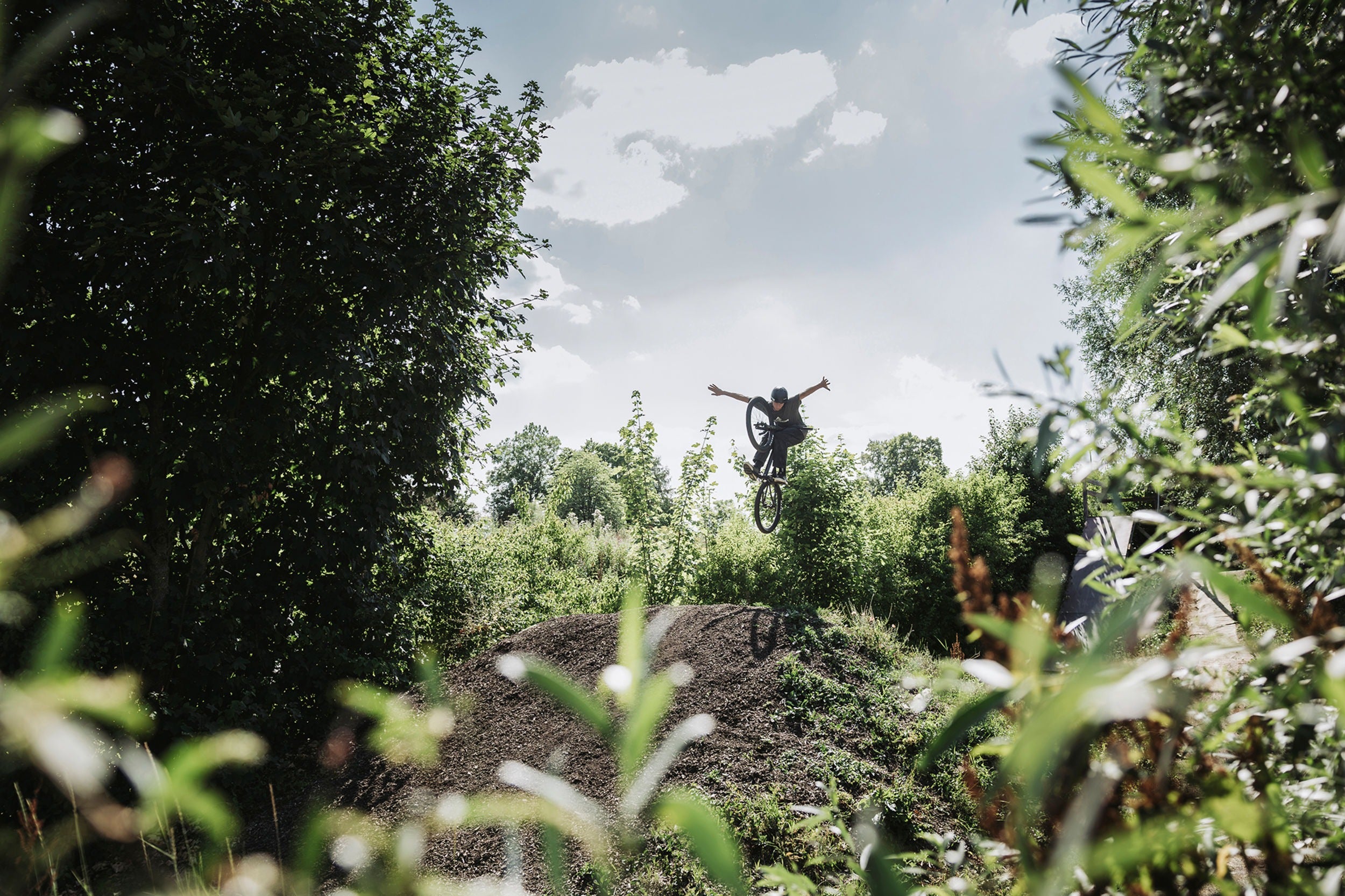 Person on a bicycle jumping over a dirt hill in a forested area