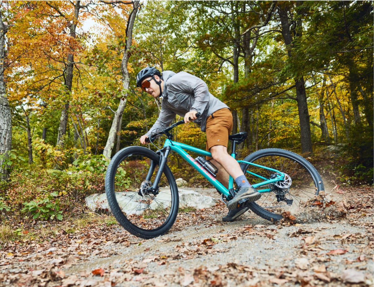 Person riding a teal mountain bike on a forest trail with autumn foliage