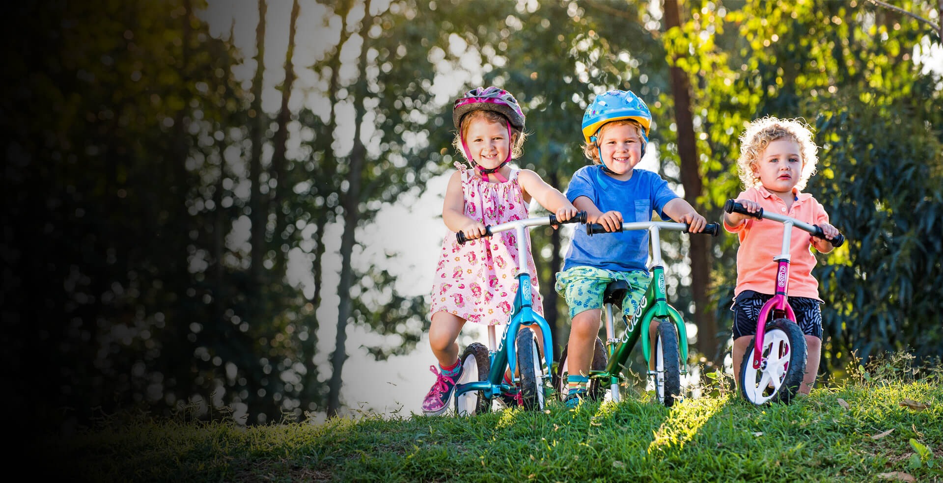 Three children on balance bikes in a park setting