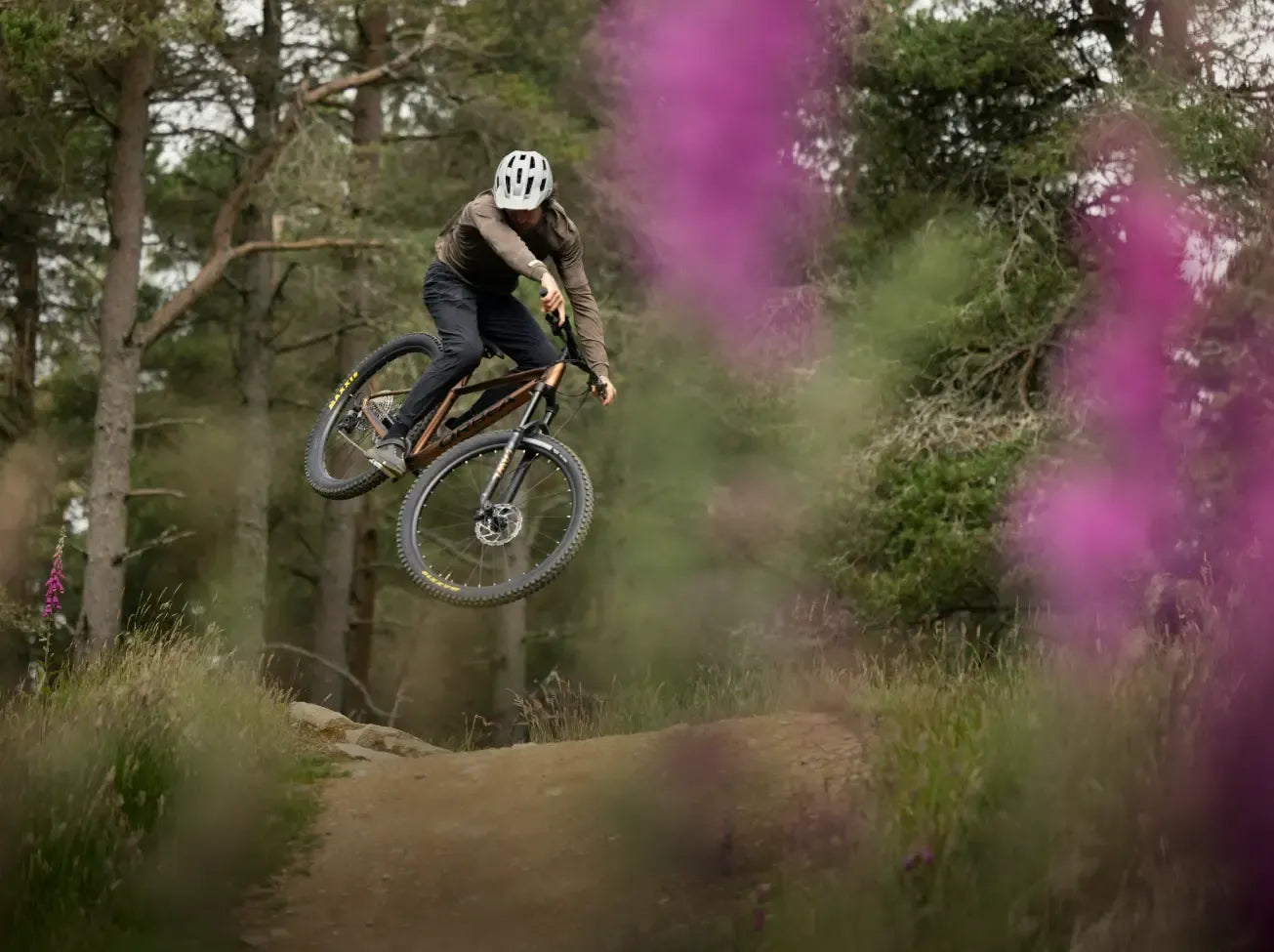 Person riding a mountain bike through a forest with purple flowers in the foreground