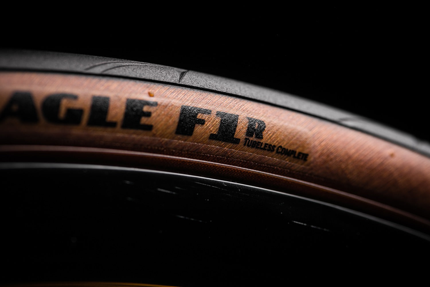 Close-up of a road bike tyre with tan wall and with 'Eagle F1' branding on a dark background