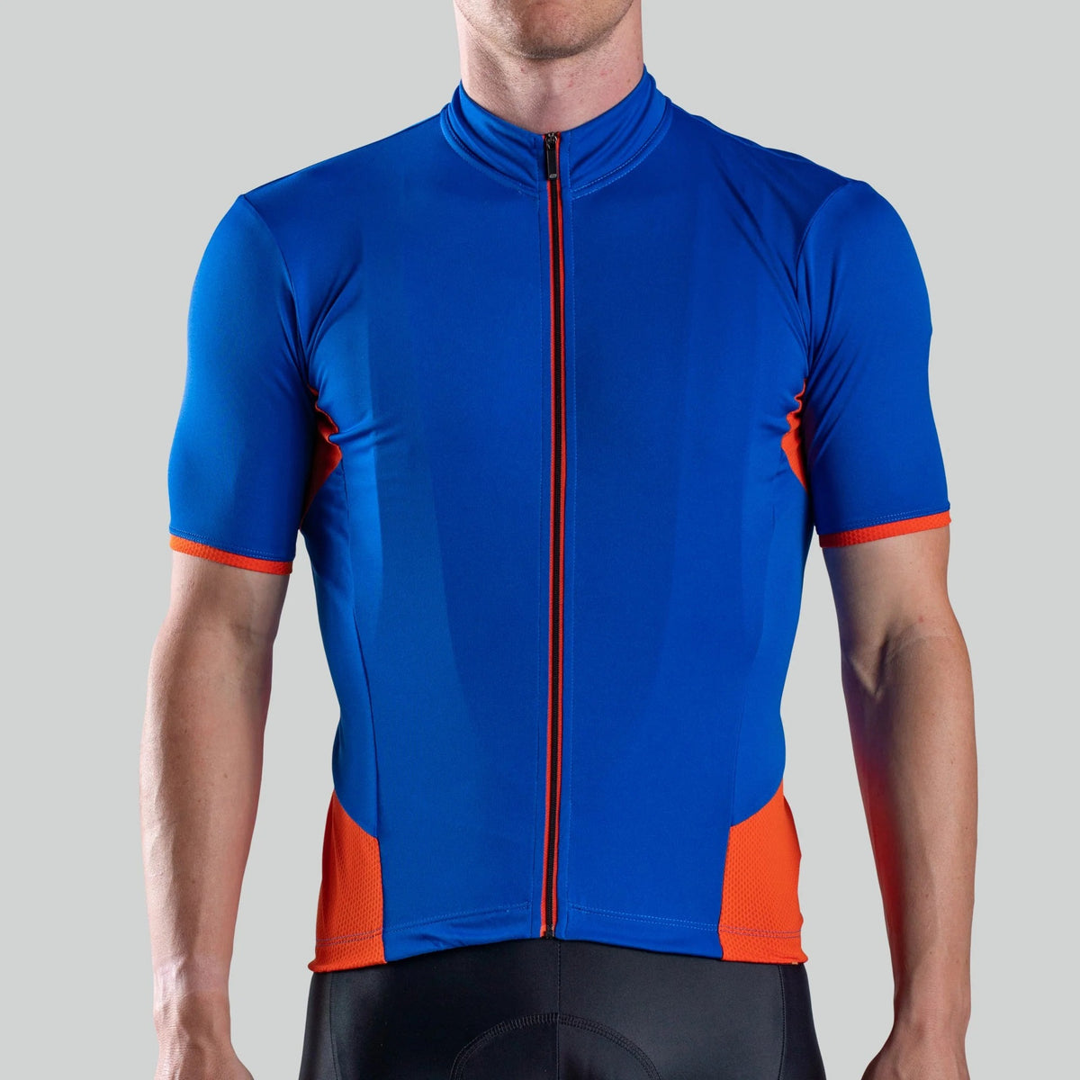 A man waring a blue cycling jersey with orange highlights and zip on a light grey background