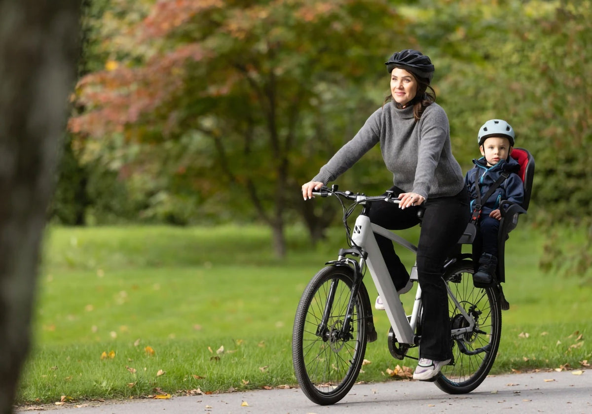 A woman riding a bike with her son in a baby seat behind her on the bike with a blurred natural background