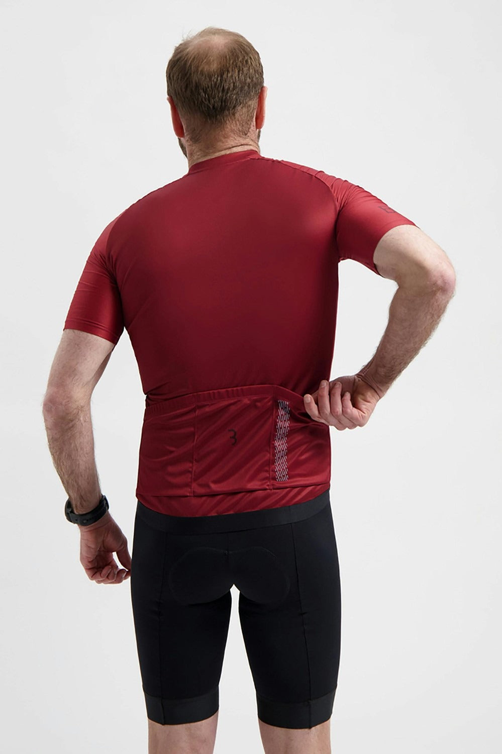 A man wearing a burgandy cycling jersey shown from behind opening his back pocket on a white background