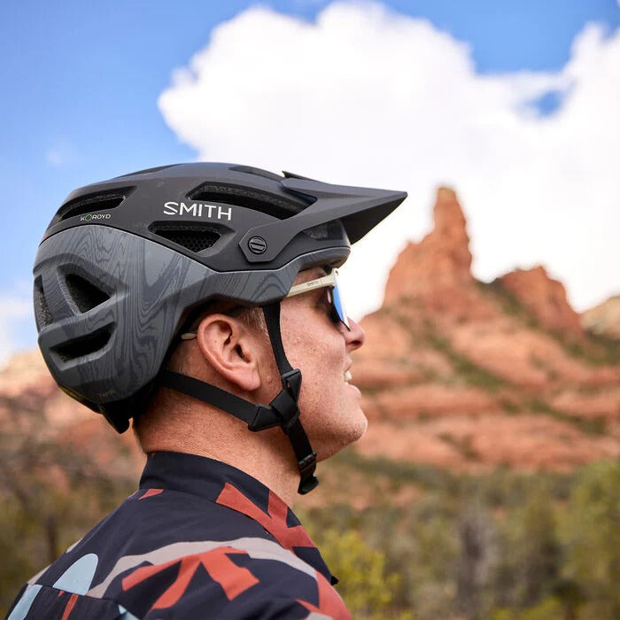 A person wearing a Smith mountain bike helmet against a blurred mountain in the background