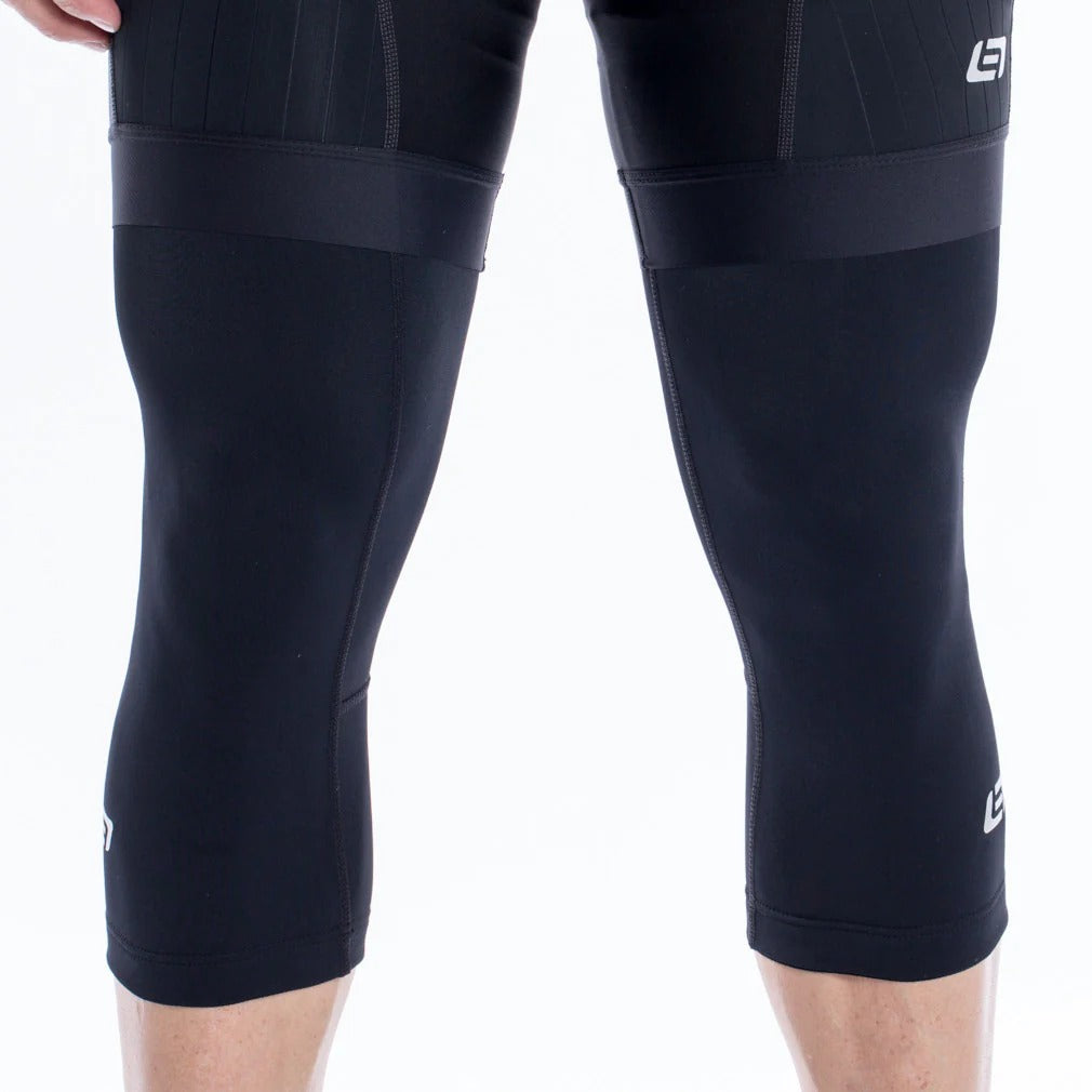 Someone wearing black cycling shorts and knee warmers with a brand logo on a white background