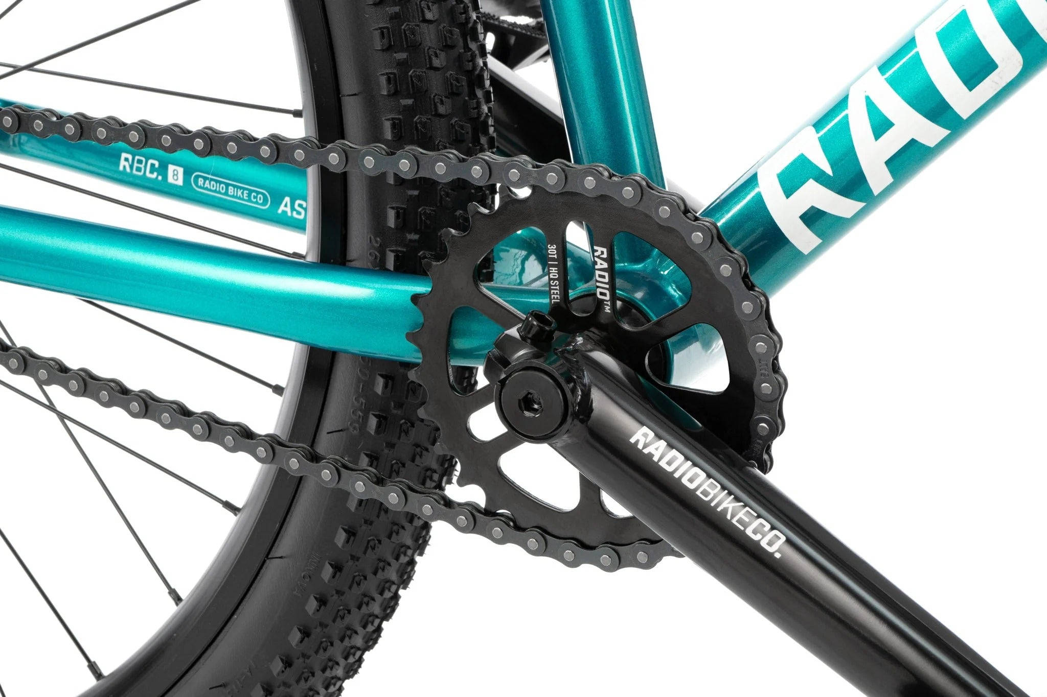 Close-up of a bicycle chain and gear system with 'Radio' branding on a teal frame.