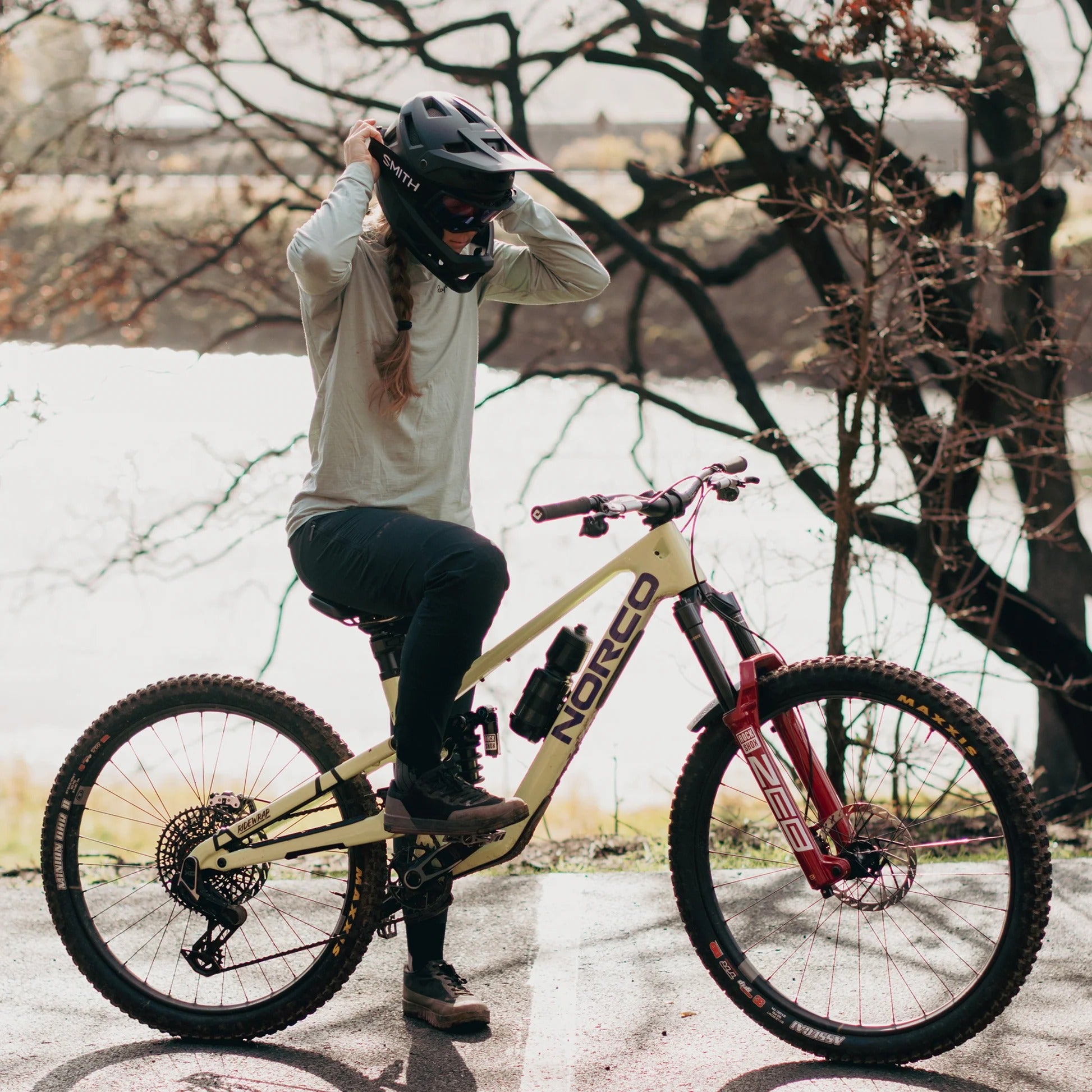 Person with a bicycle in an outdoor setting, wearing a black Smith full face mountain bike helmet helmet.