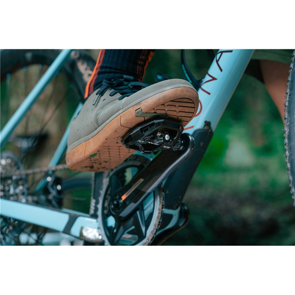 Close-up of a foot wearing a gray shoe with brown sole clipped into a bicycle pedal.
