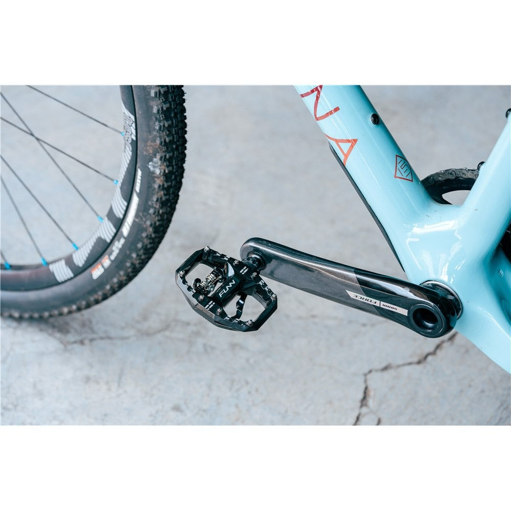 Close-up of a bicycle pedal and chain on a light blue frame with a white background.