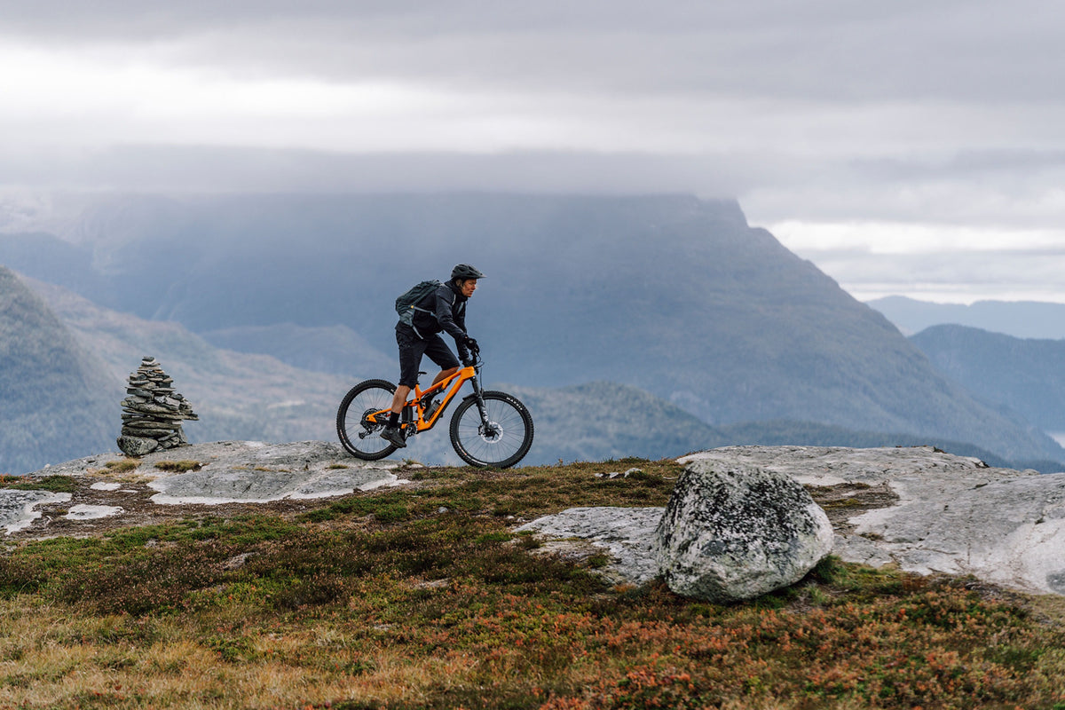 A mountain biker riding an orange dual suspension mountain bike in the mountains