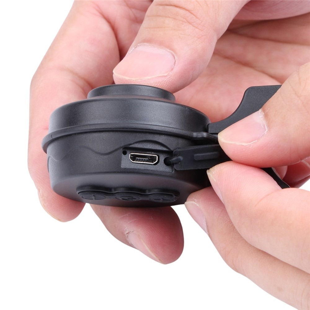Hand holding a small black bicycle bell with USB connector on a white background