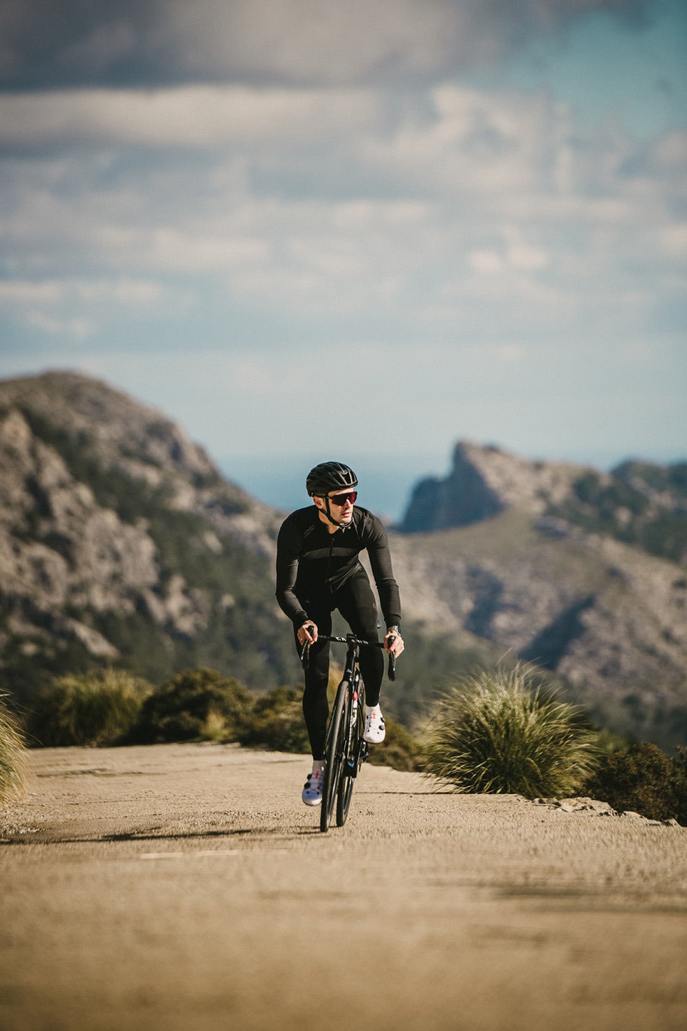 Person cycling on a mountain road with scenic mountains in the background