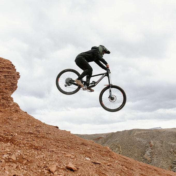 Person on a mountain bike performing a jump in a desert landscape with a cloudy sky.