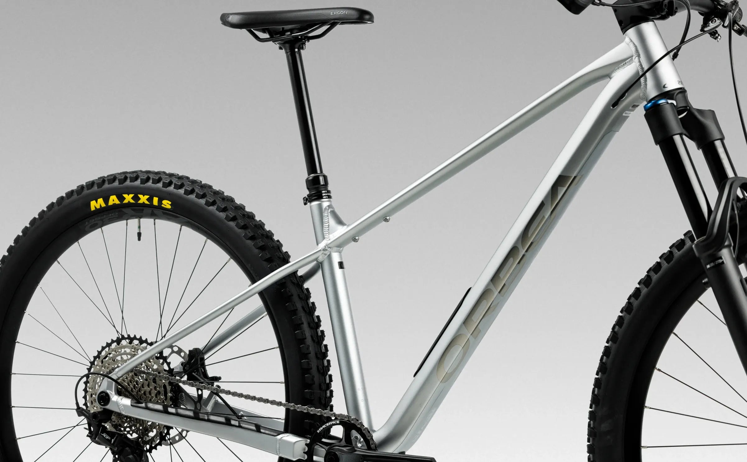 Silver Orbea mountain bike with Maxxis tyres on a gray background