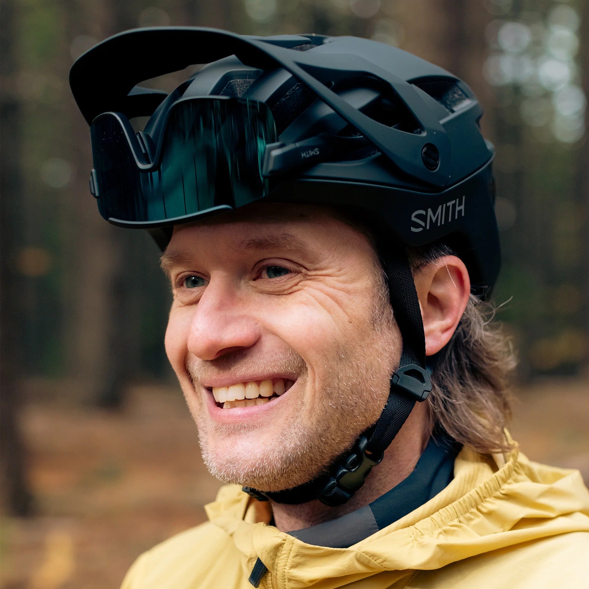 Man wearing a black Smith helmet and yellow jacket in a forest setting