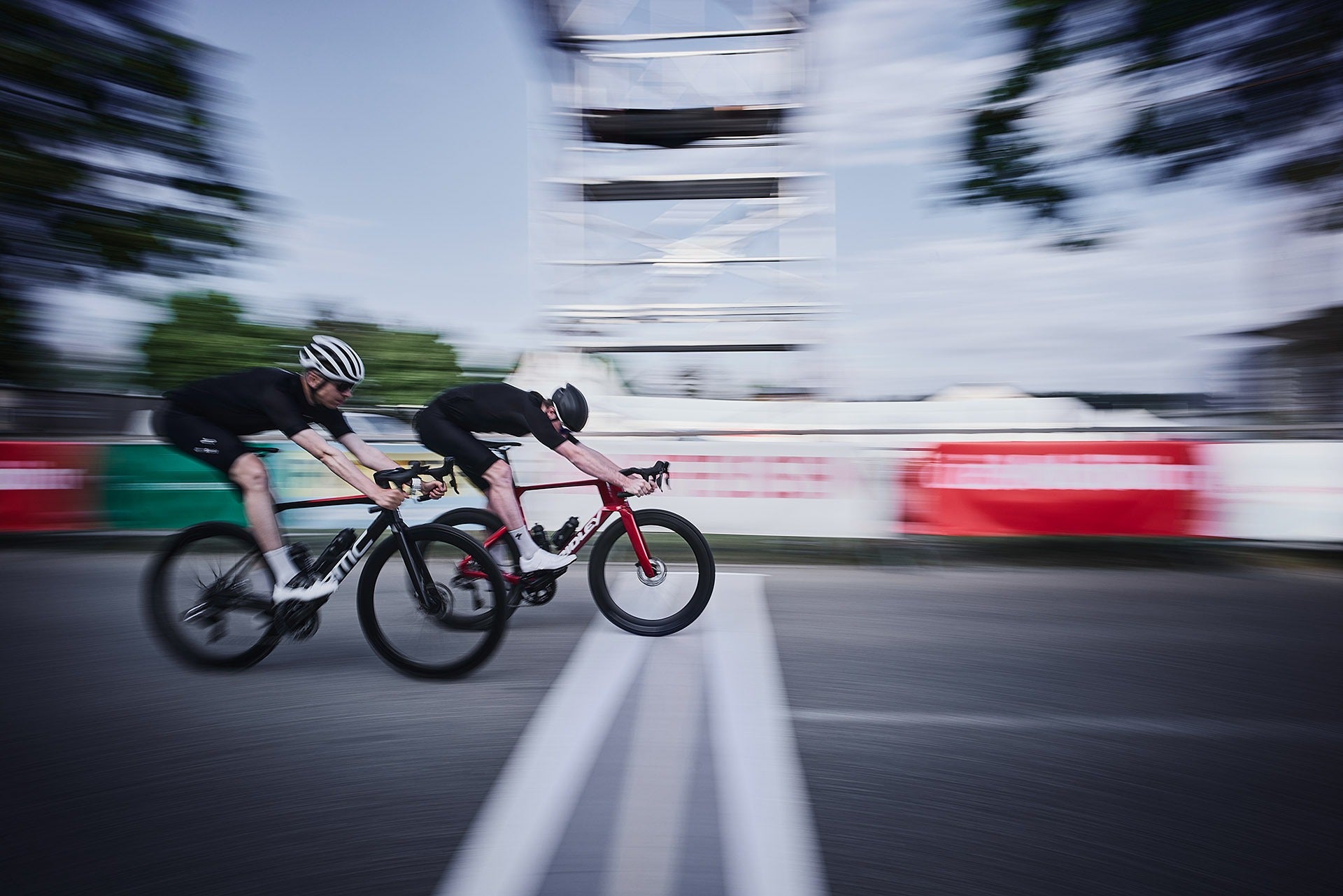 Two cyclists racing on a blurred road with buildings in the background