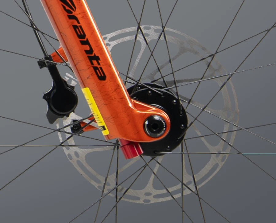 Close up of the front fork and disc rotor of an orange mountain bike with 'Branta' branding down the front fork on a light grey background