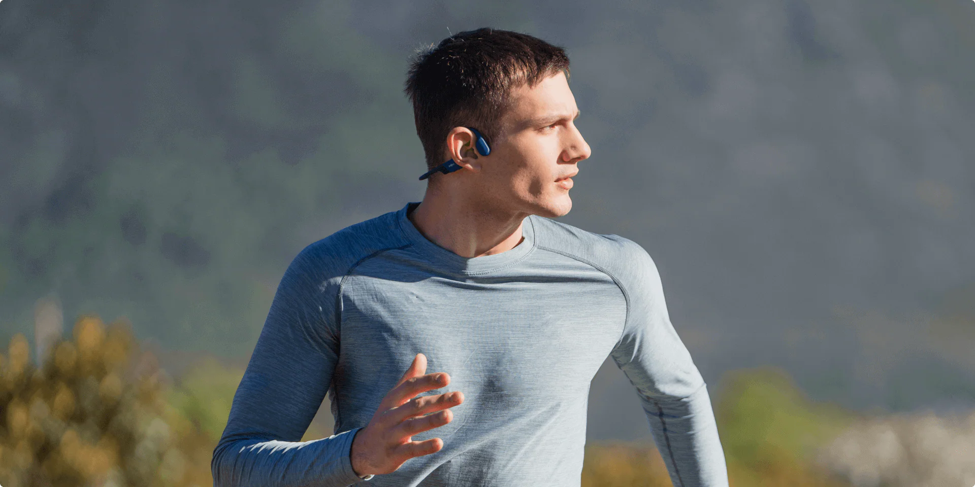 Man running outdoors with mountains in the background wearing wireless headphones