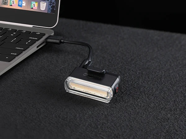 USB rear bicycle light attached to a laptop on a dark surface