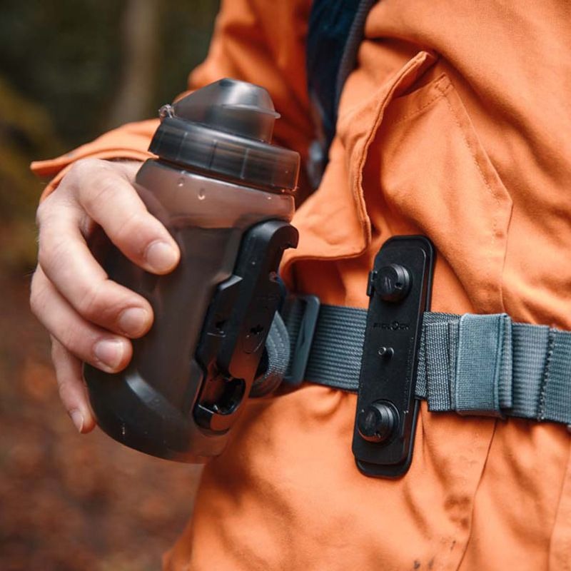 Person holding a black water bottle with a forest background