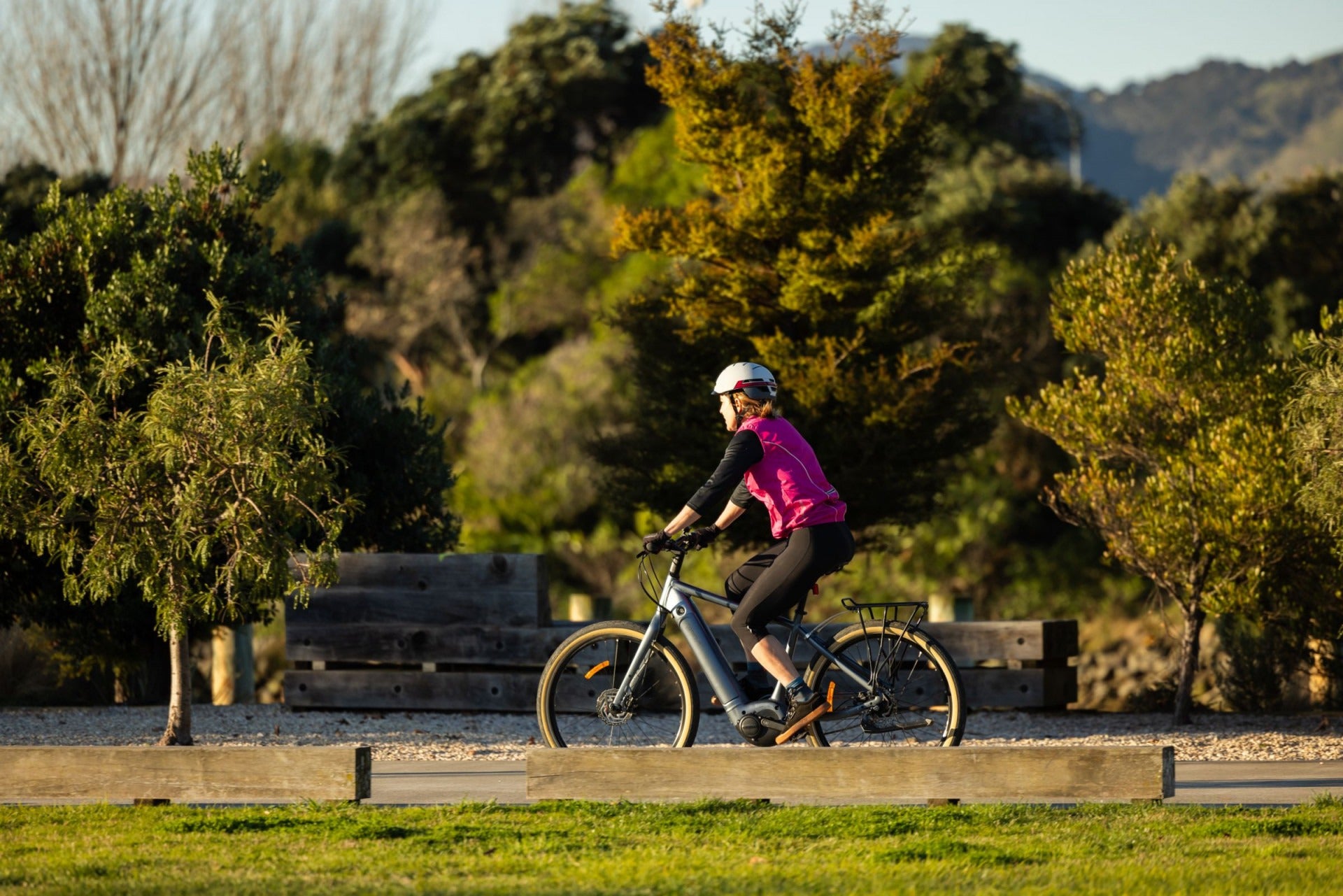 Person riding a bicycle in a park with trees and a bench in the background