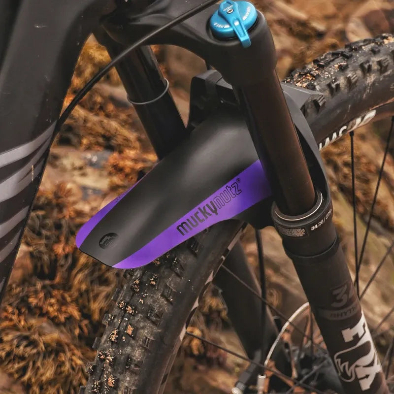 A close up of a Mucky Nuts black and purple face fender mudguard installed on a mountain bike against an outdoor background