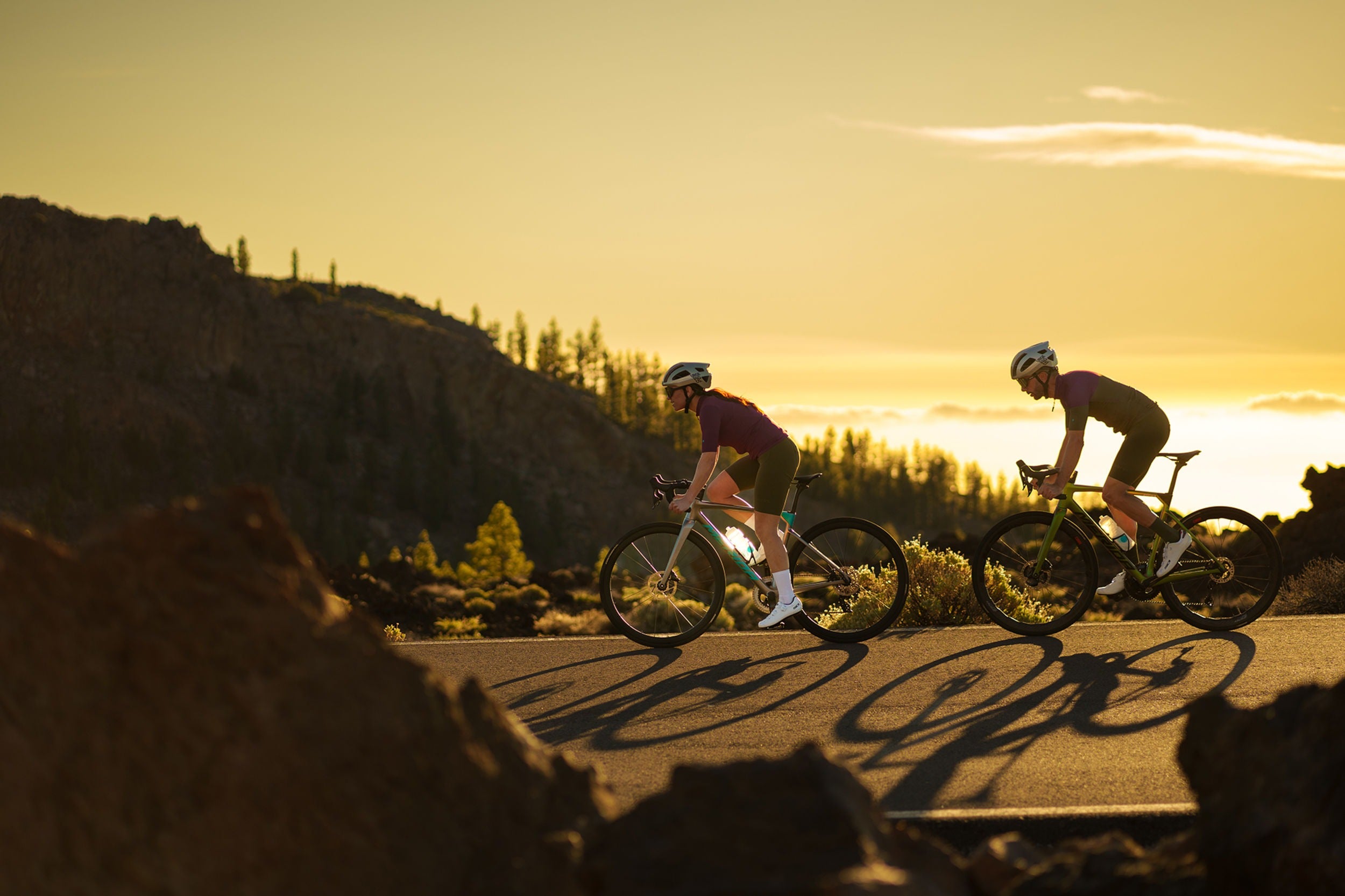 Two cyclists riding on a road during sunset with mountains in the background.