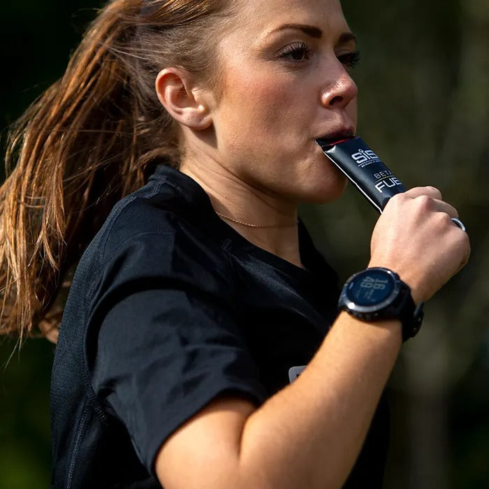 Woman drinking from a SIS energy gel with a blurred natural background