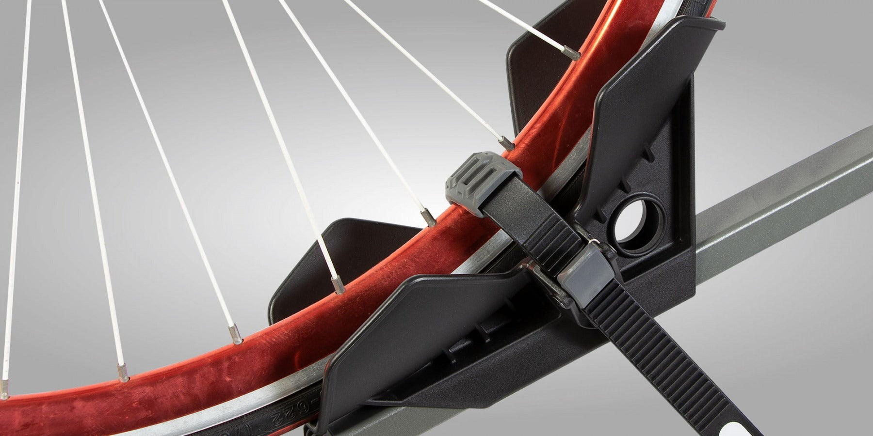 Close-up of a bicycle wheel with a red rim and black tyre seated into a bike rack strapped in on a gray background