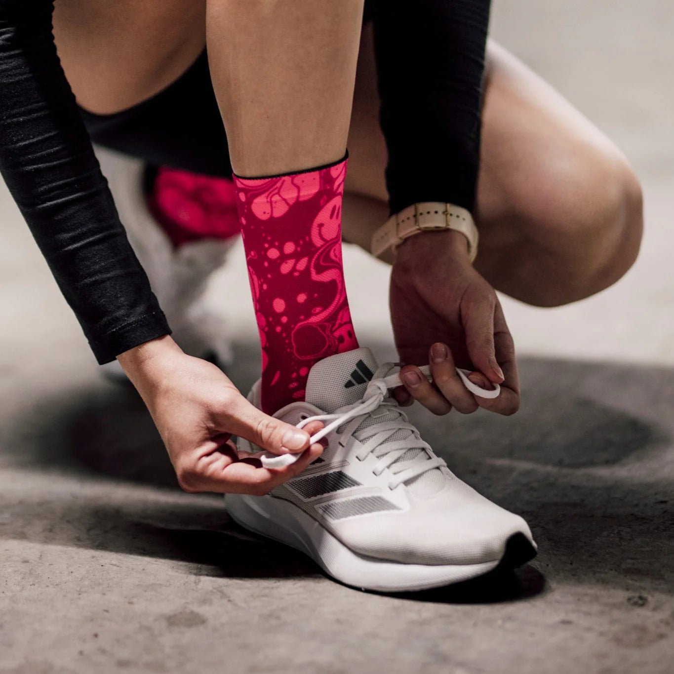 A lady tying her shoe lace on a white trainer with bright pink socks with a concrete floor in the background