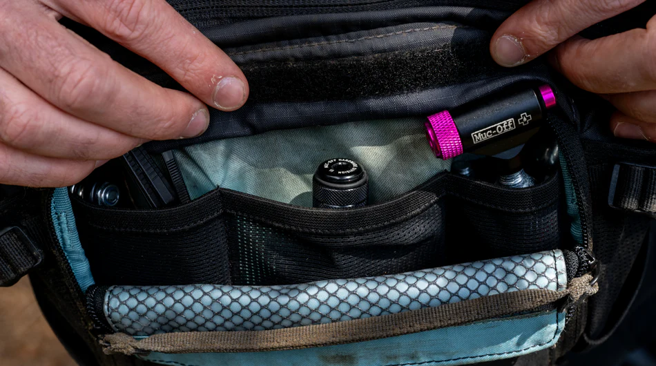 Person opening a black bicycle bag to reveal the Muc-Off Precision Tubeless Repair Capsule Tool inside.