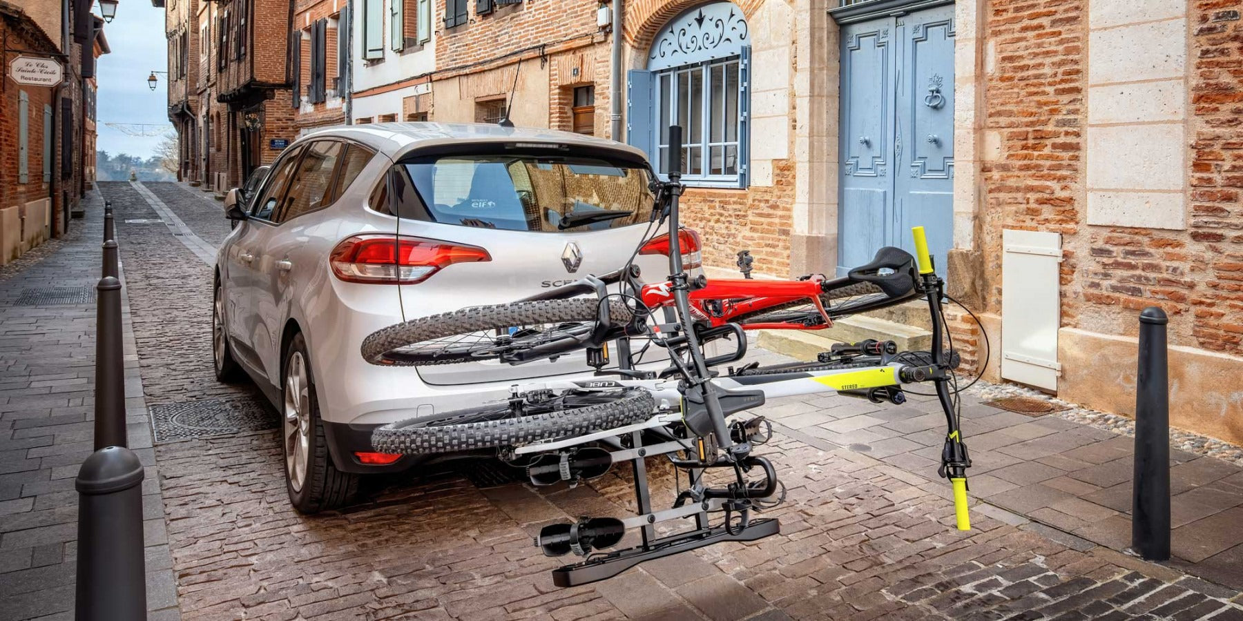 White car with a bike rack on a narrow street in an urban setting