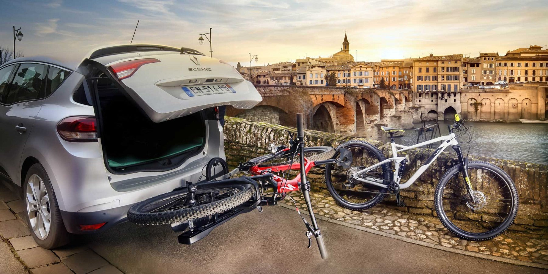 Car with open trunk and bicycles attached, cityscape in the background