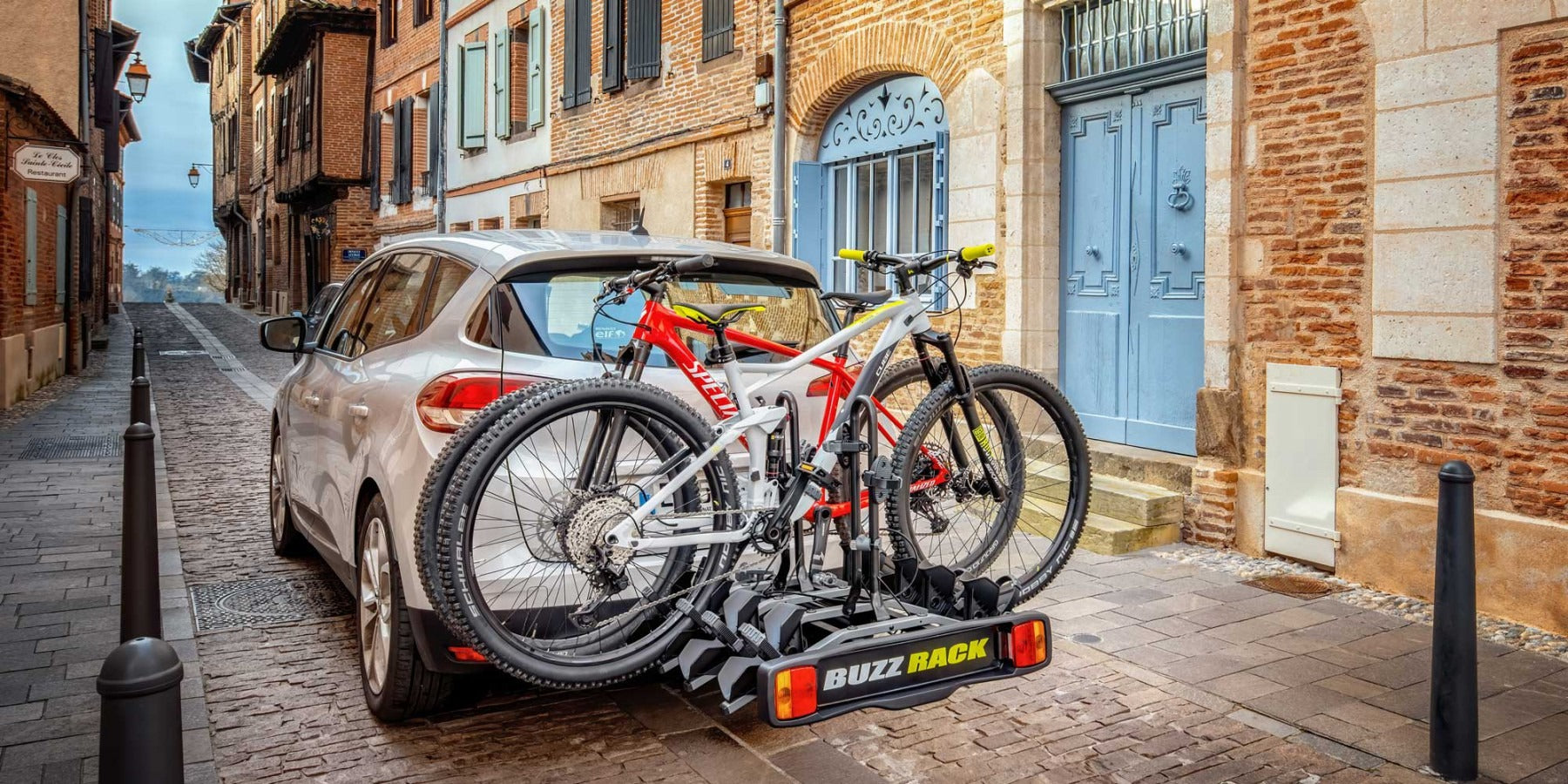 Buzz Rack bike rack on a car with two bikes attached parked in a narrow street