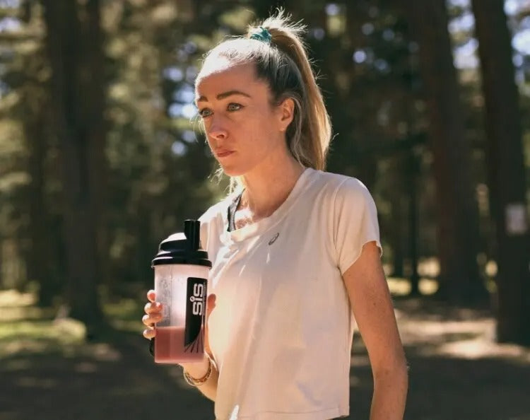 Woman holding a protein shake container in a forest setting