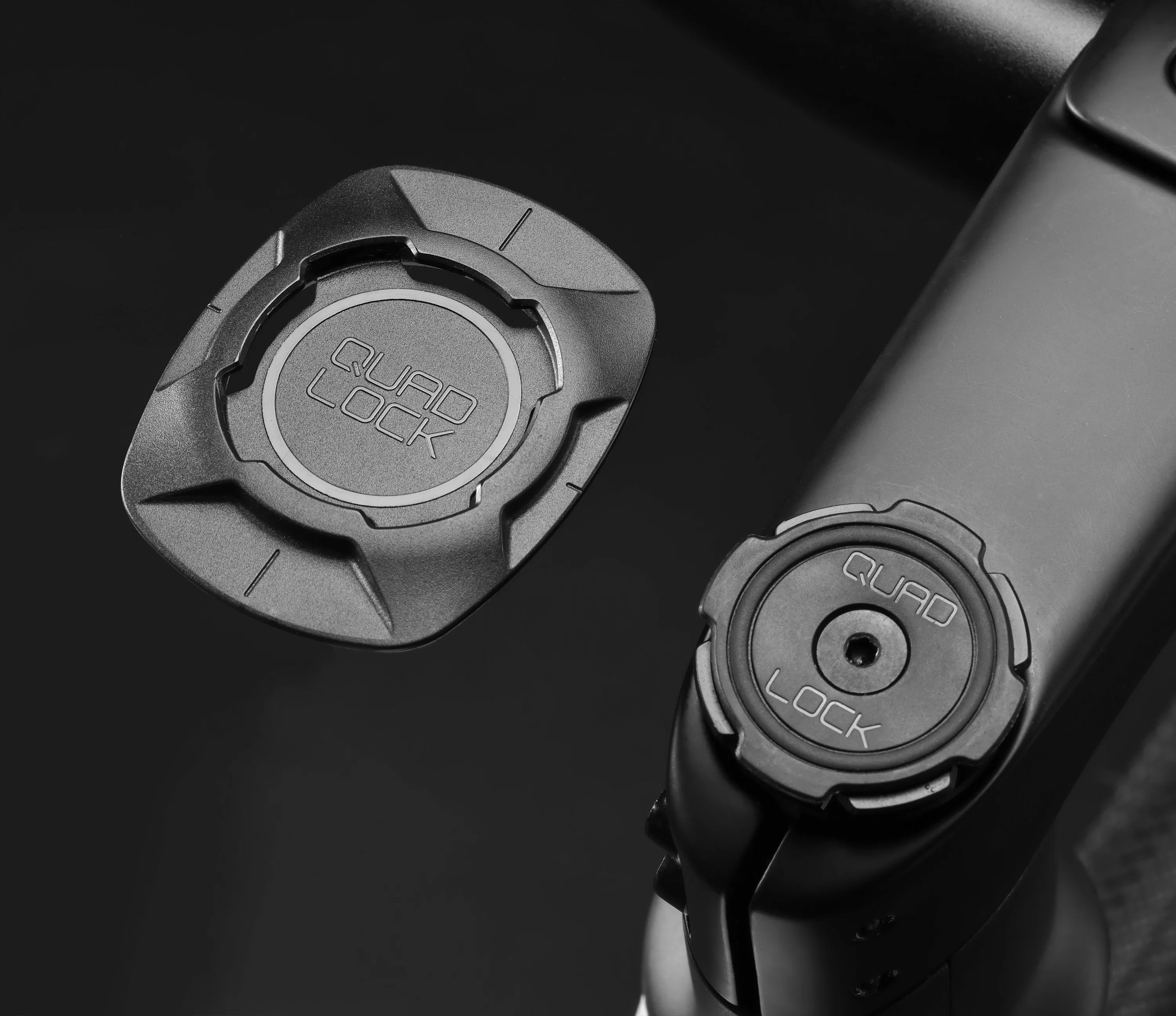 Two Quad Lock phone mount attachments on a black background