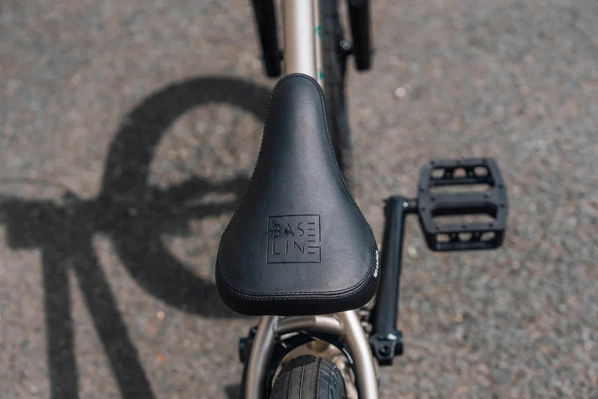 Close-up of a BMX Bicycle seat with 'BASE LINE' branding on a road surface.