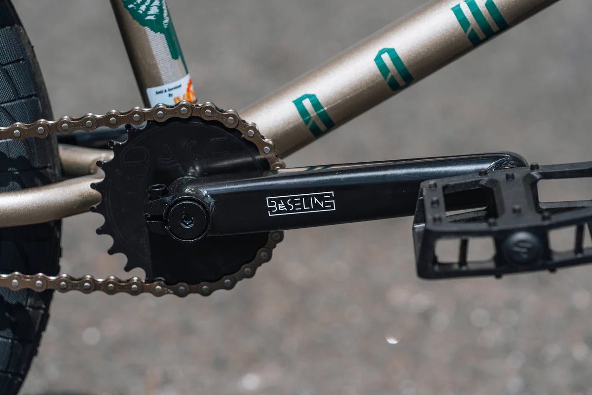 Close-up of a BMX Bike chain and gear system with 'Basoline' branding on the crank on a blurred background