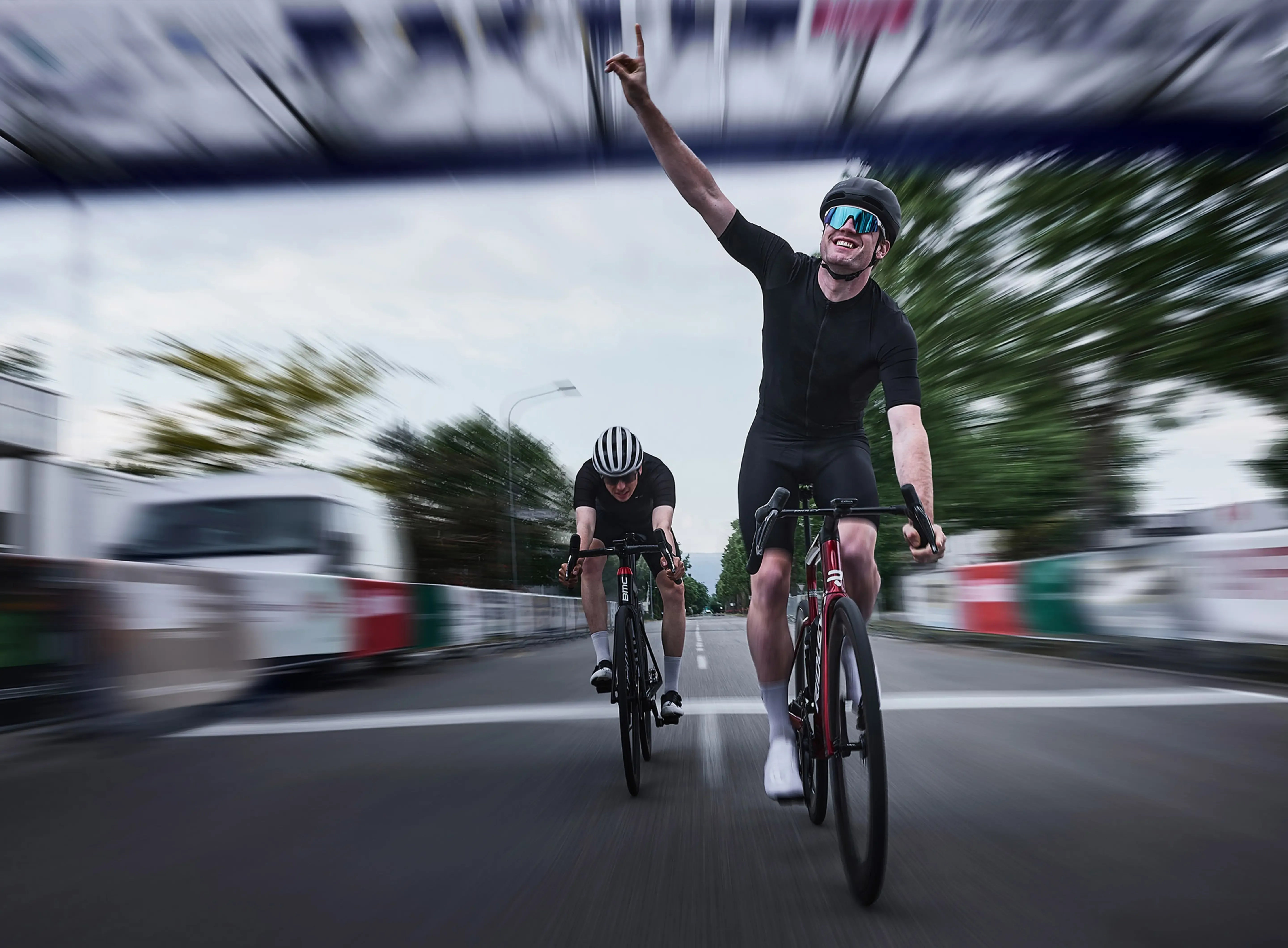 Cyclist celebrating victory on a road bike with another cyclist in the background.