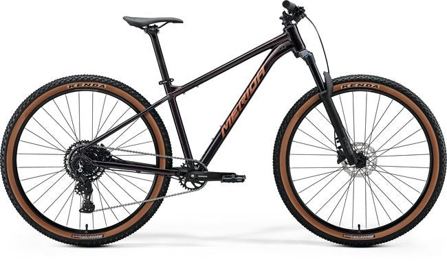 A black Merida hardtailmountain bike with brown sidewall tyres, shown from a side profile on a white background.