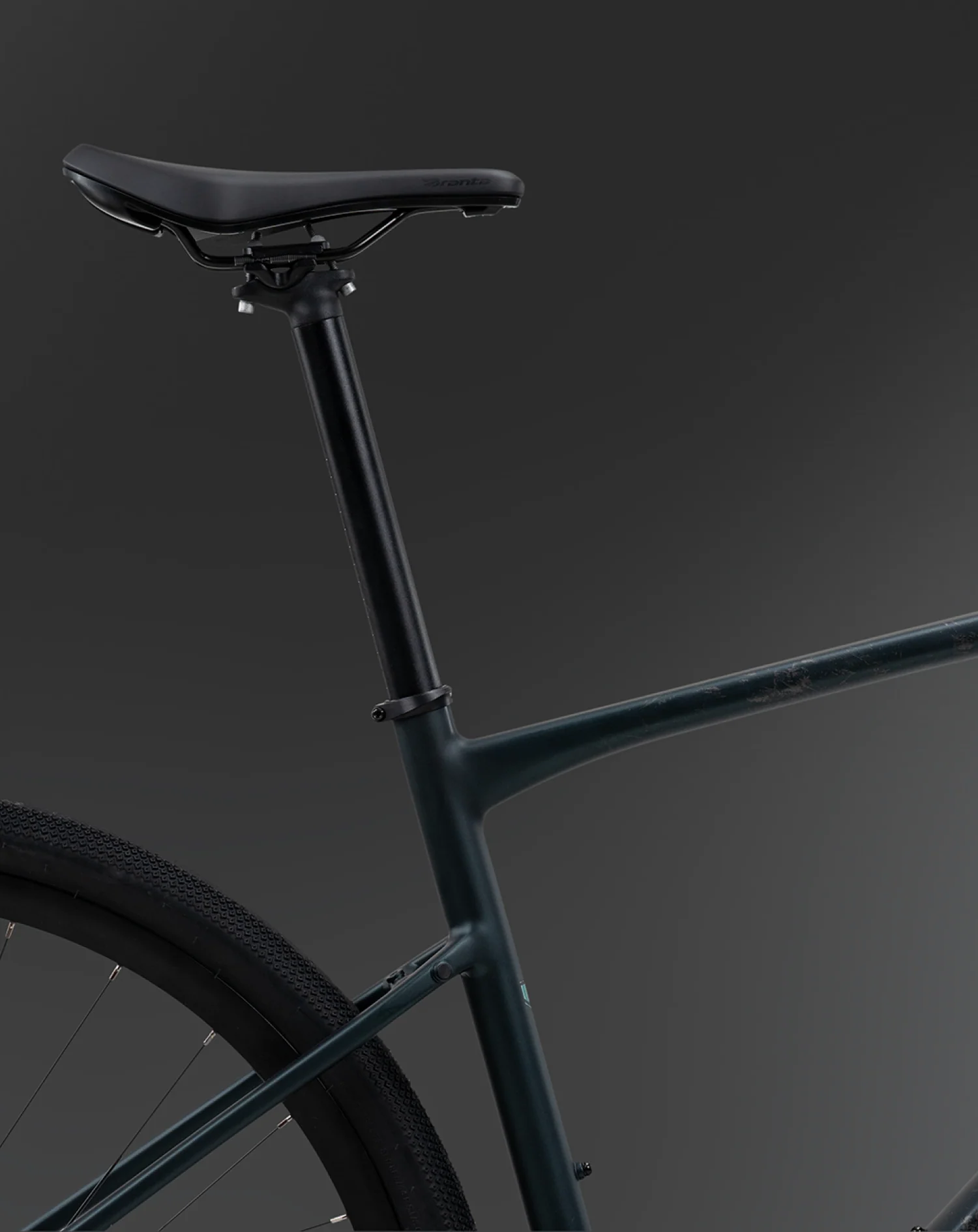 Close-up studio shot of a bicycle frame and saddle in matte black against a dark gray gradient background.