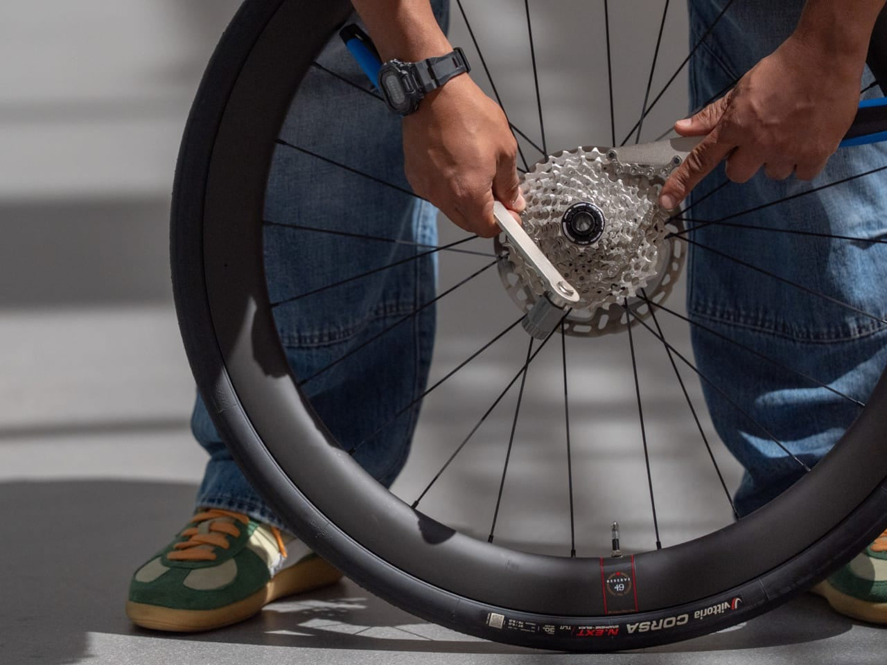 Person removing a cassette on a bicycle wheel using two tools against a neutral background